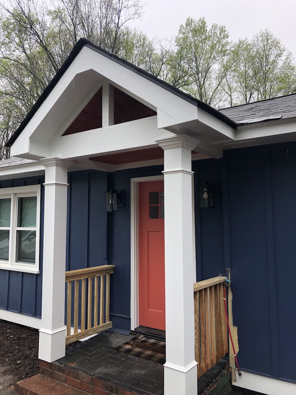 White portico with railing on it in the dark house with red door